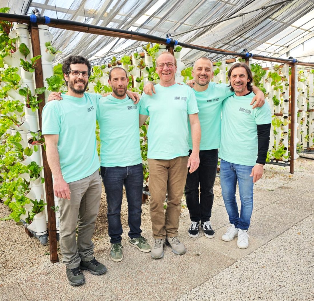 Cinque persone del team di Nonna Futura, sorridenti, con la maglietta del marchio davanti alle colonne di insalate in serra